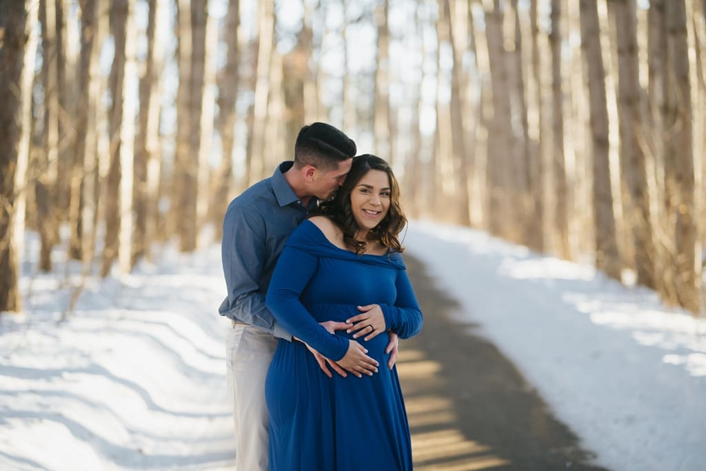 expecting couple embraces in snowy woods
