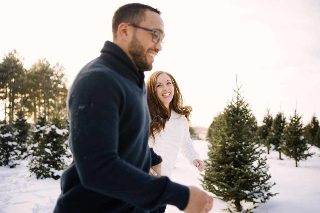 couple running through snow at tree farm
