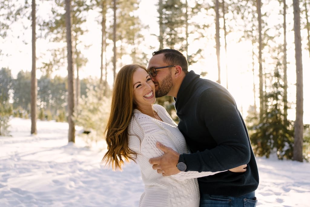 man kisses woman's cheek in snow at sunset